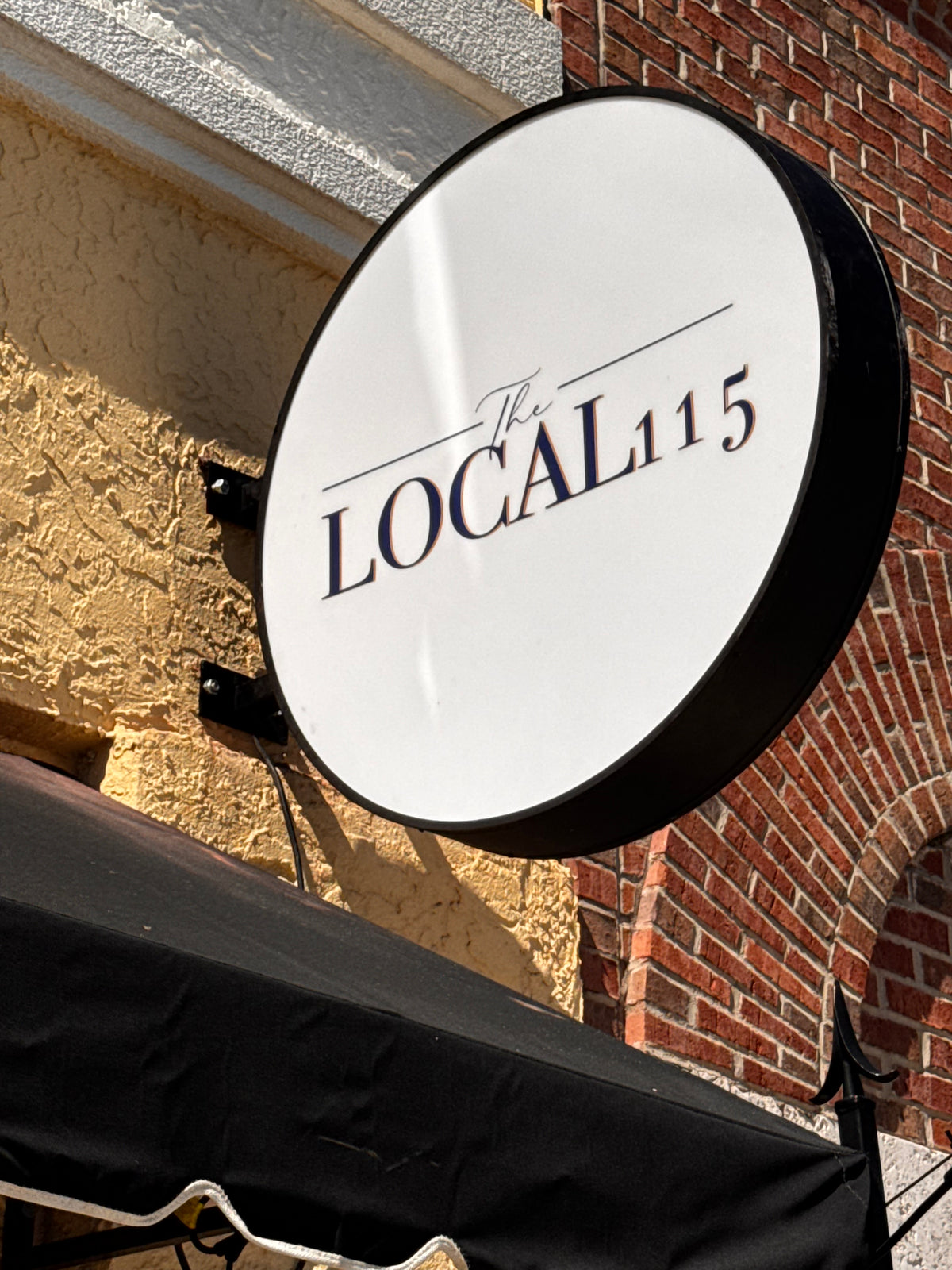 LOCAL 115 round blade sign above a storefront
